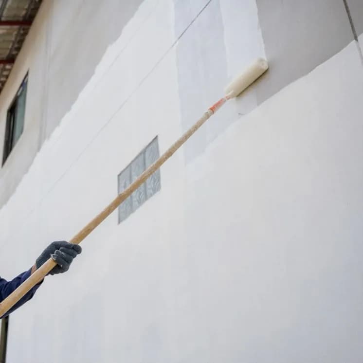 Painter rolling white paint onto an exterior wall