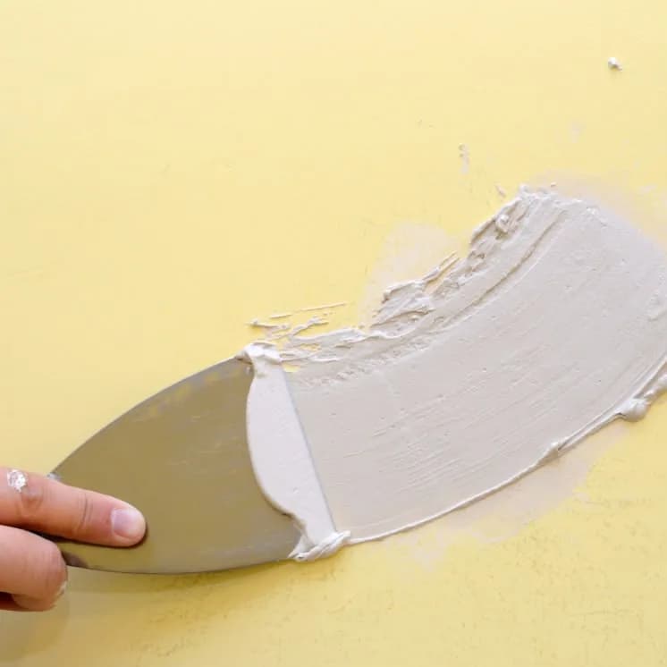 Spatula spreading wall putty over a yellow wall