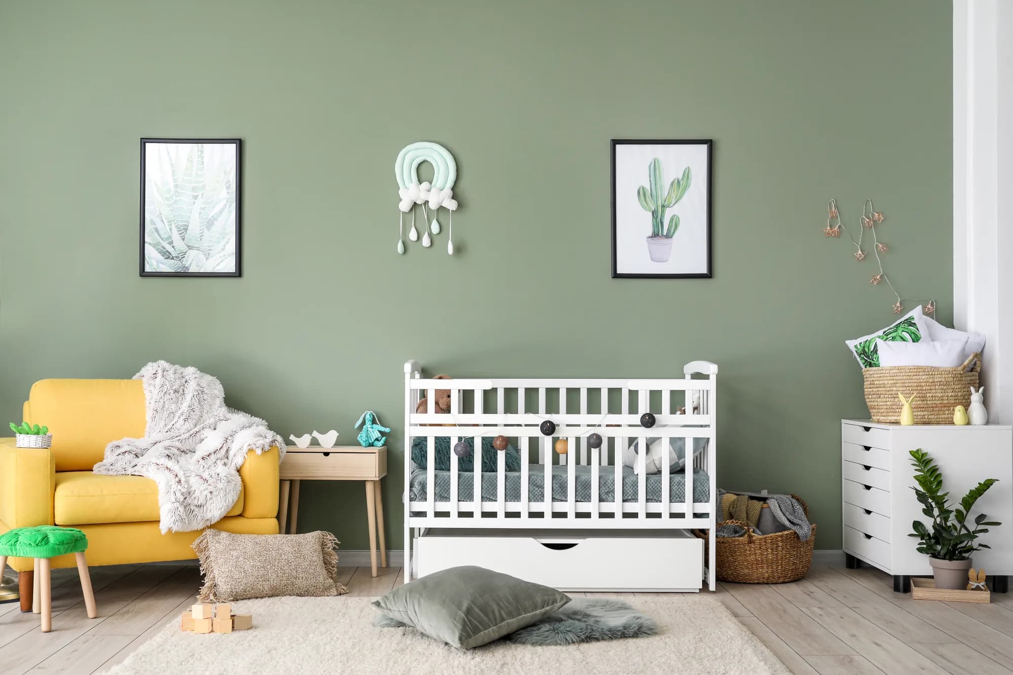 Nursery with a sage green wall, crib and yellow armchair
