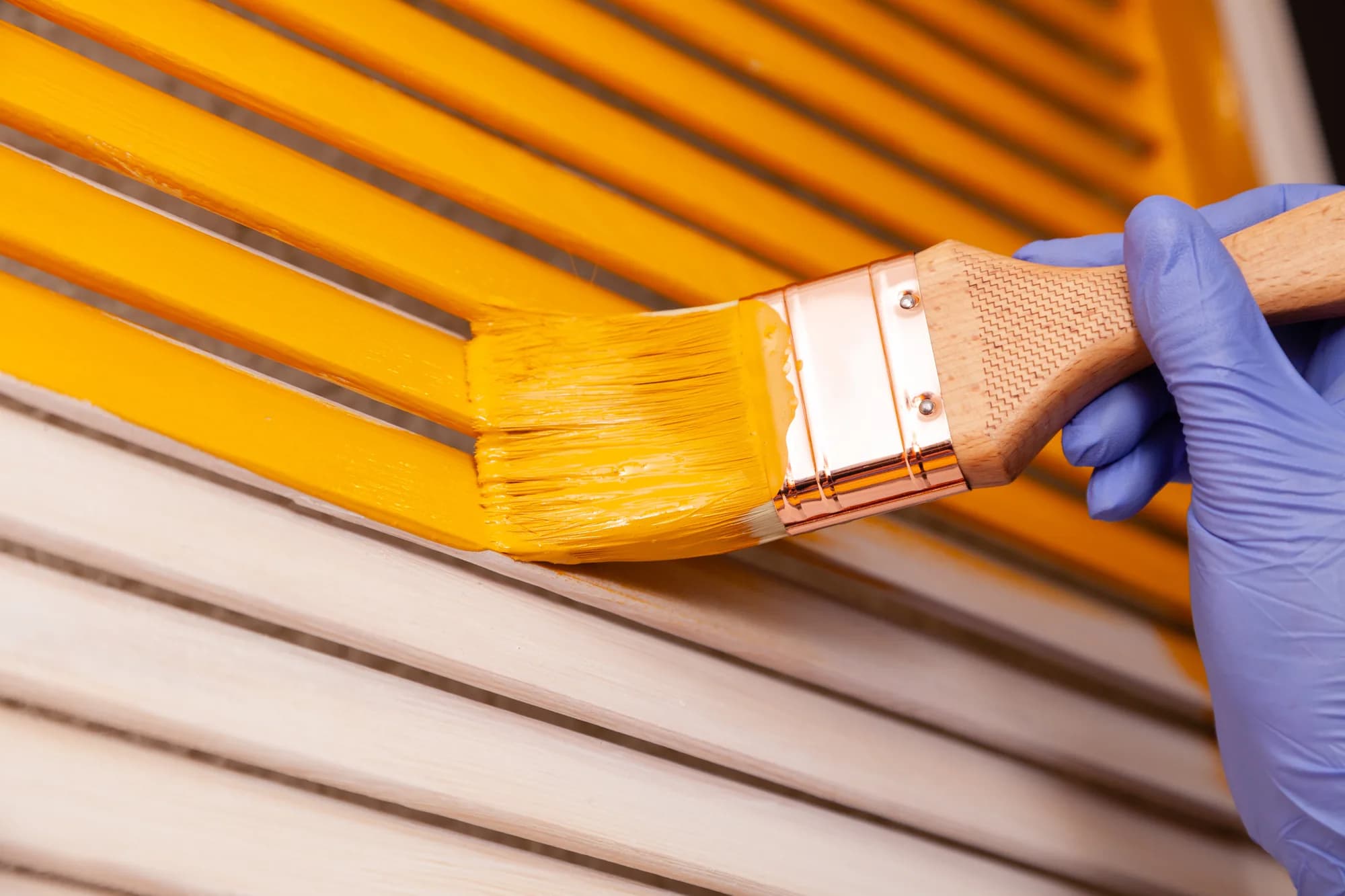 Brush applying yellow paint to wooden slats